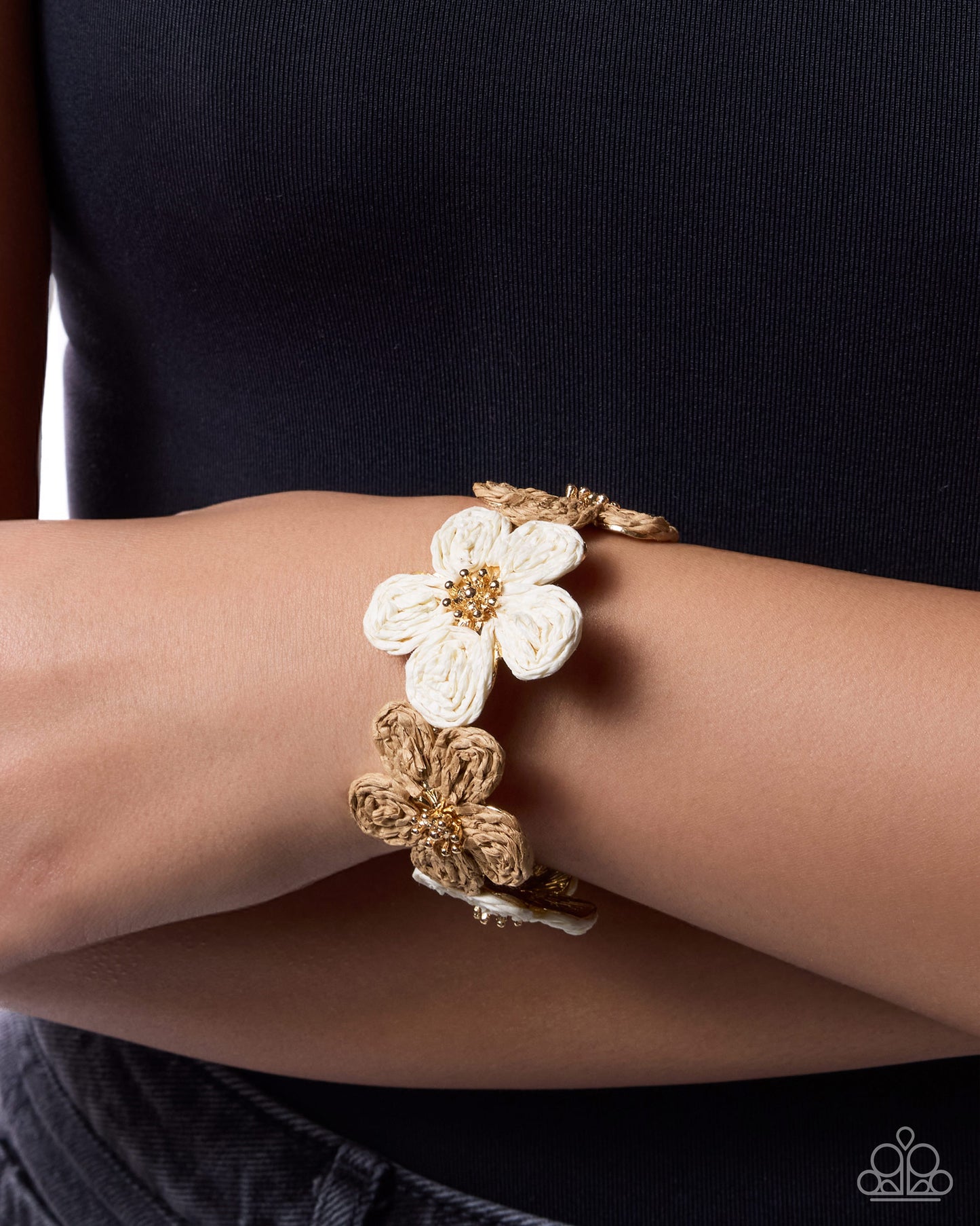 Gold bracelet with a white flower on a wrist against a black background