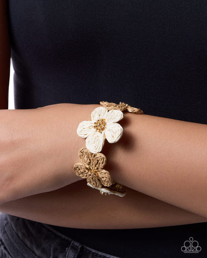Gold bracelet with a white flower on a wrist against a black background
