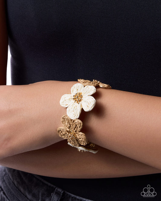 Gold bracelet with a white flower on a wrist against a black background