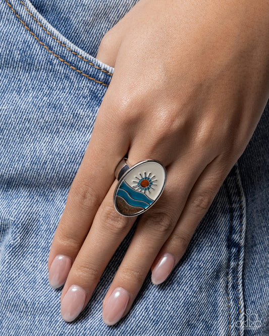 Hand wearing a ring with a sun and wave design on denim fabric