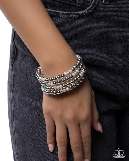 Stack of silver beaded bracelets on a wrist against a dark background