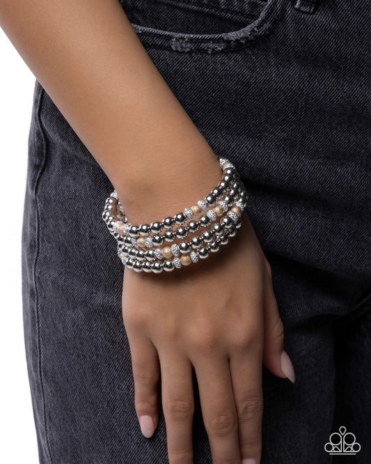 Stack of silver beaded bracelets on a wrist against a dark background