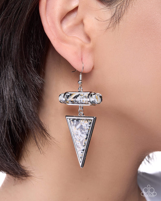 Close-up of an ear wearing a silver triangle-shaped earring with a blurred background