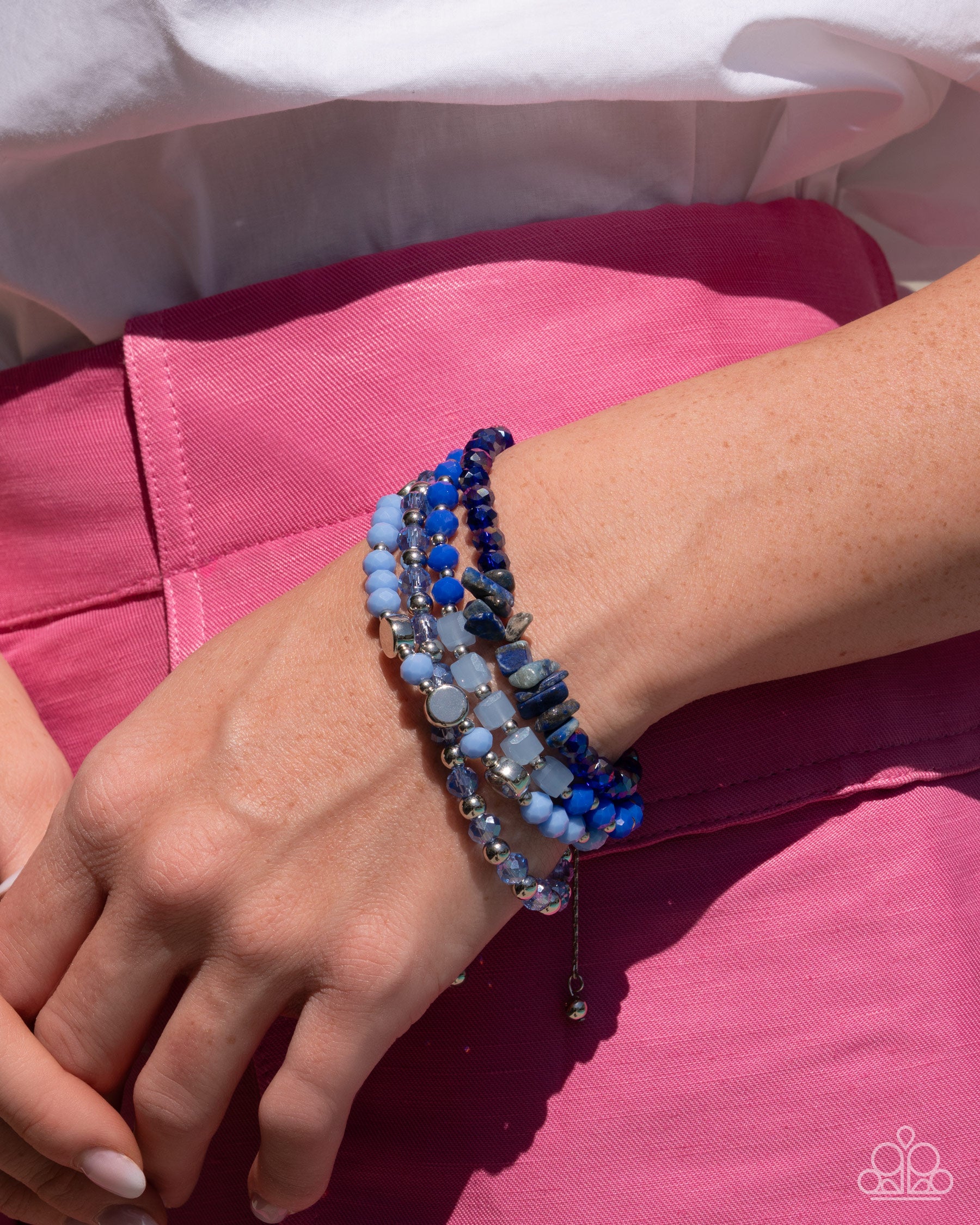 Close-up of a wrist wearing multiple blue beaded bracelets on a pink fabric background