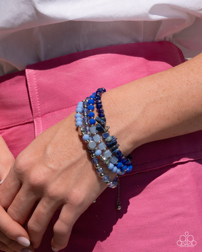 Close-up of a wrist wearing multiple blue beaded bracelets on a pink fabric background