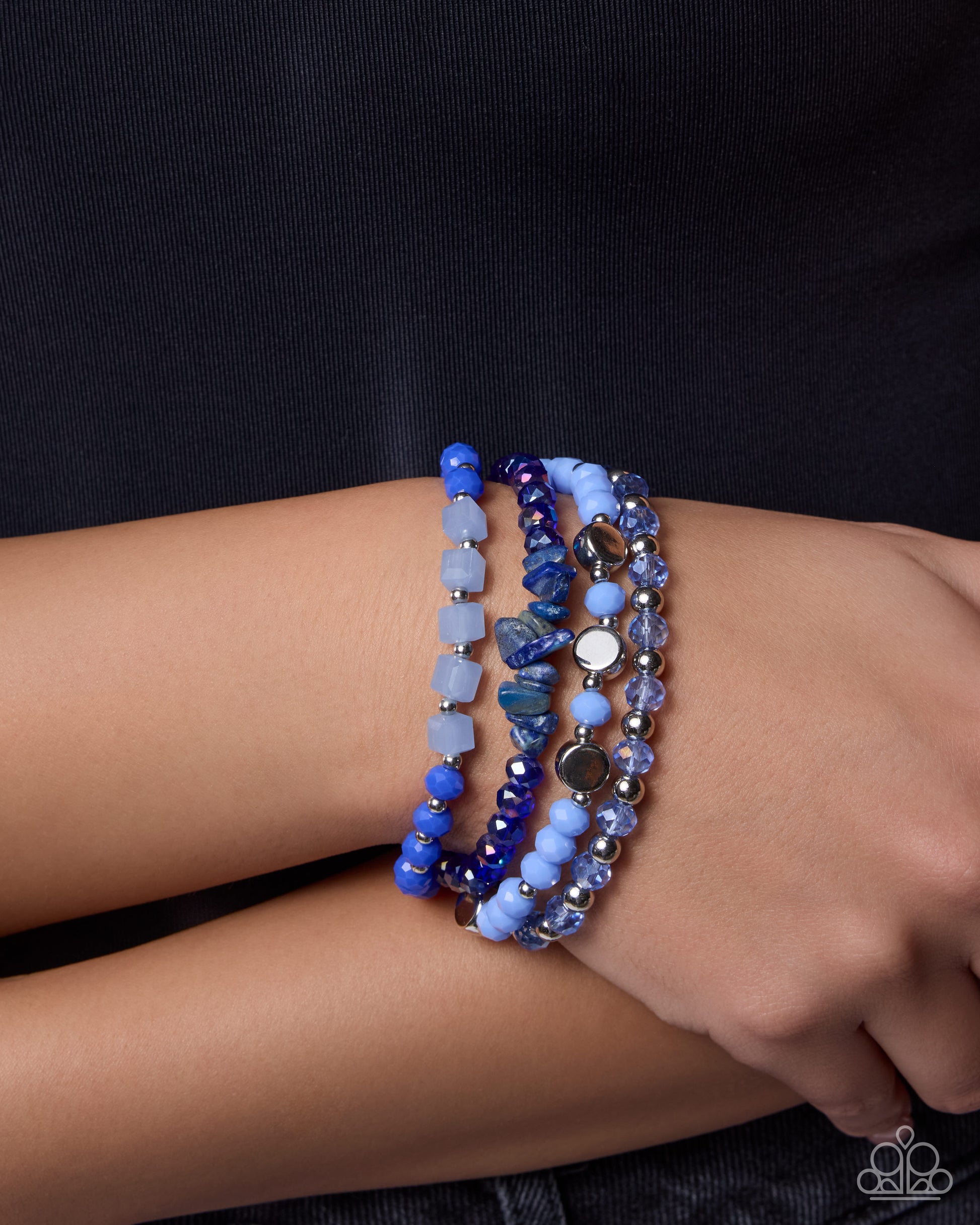 Stack of blue beaded bracelets on a wrist against a dark background