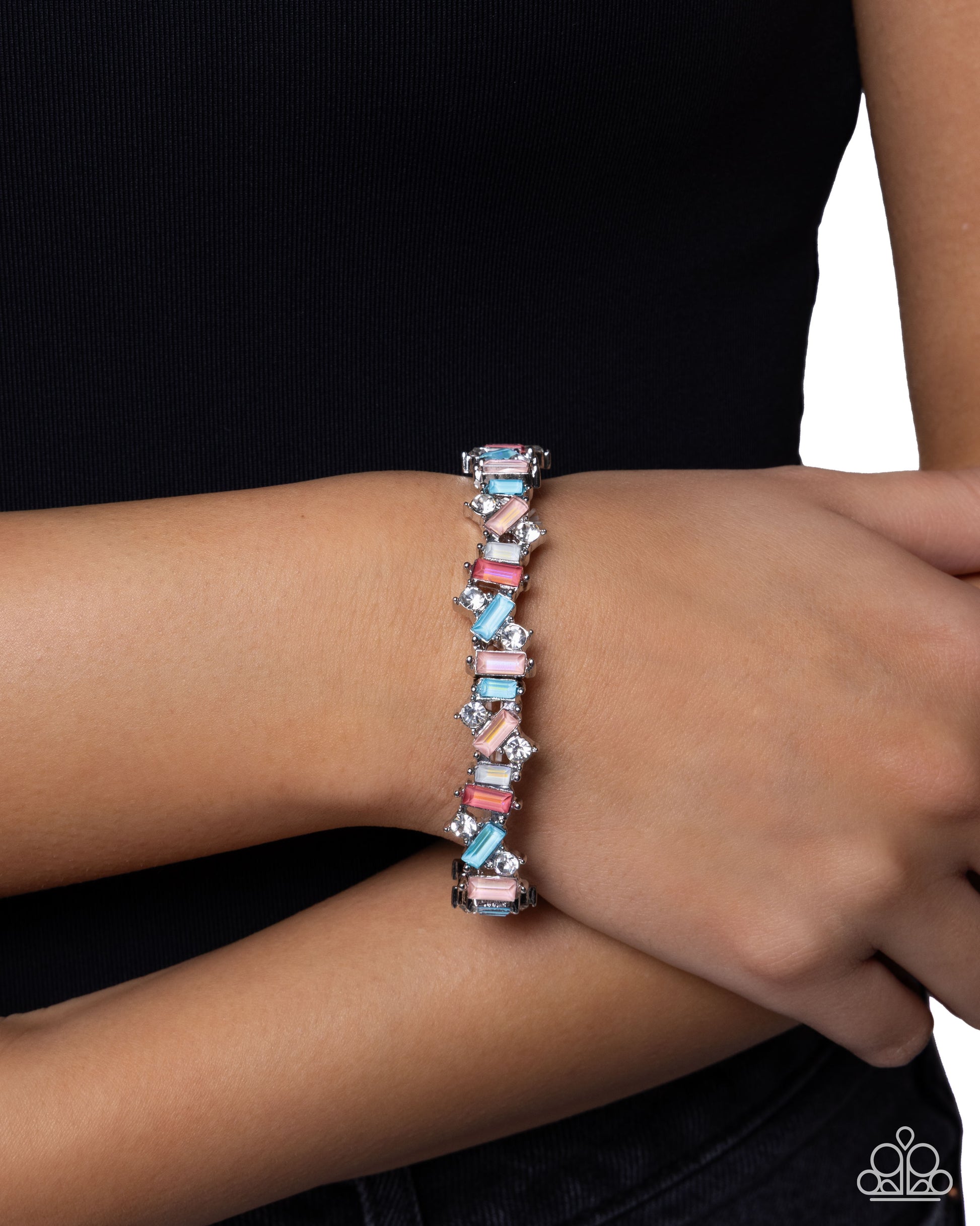 A close-up of a person's wrist wearing a silver-toned stretch bracelet adorned with alternating pastel pink, light blue, and white rectangular charms.