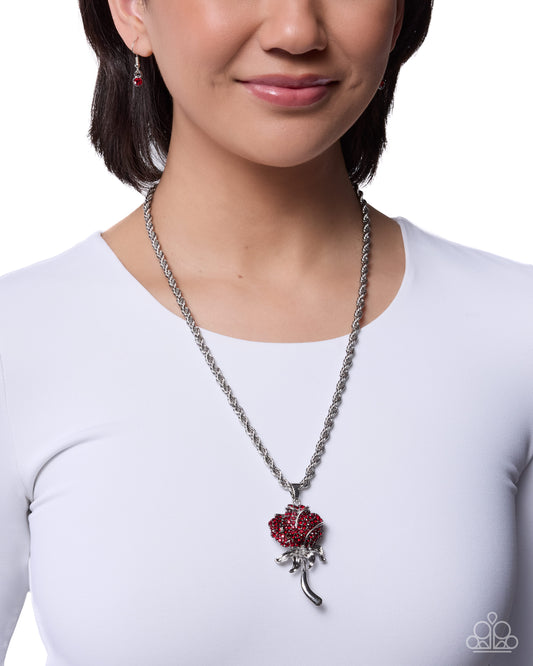 Person wearing a silver necklace with a red flower pendant on a white background