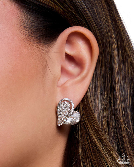 A close-up of a model's ear wearing a silver-toned teardrop-shaped stud earring encrusted with clear crystals, with her brown hair visible against a white background.
