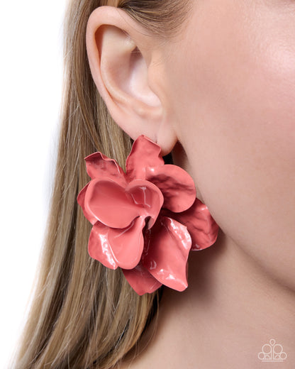 Pink flower-shaped earring worn by a person with blonde hair.