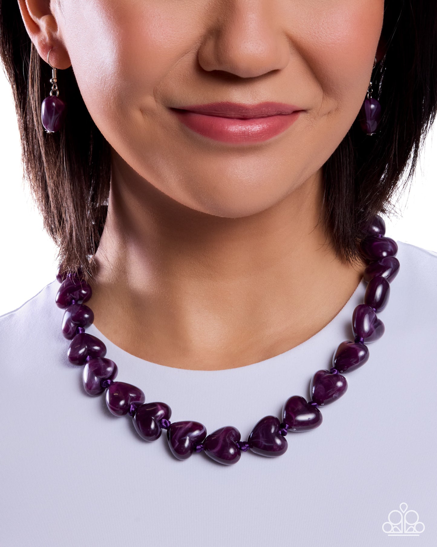 Close-up of a woman wearing a purple heart-shaped necklace and earrings on a white background
