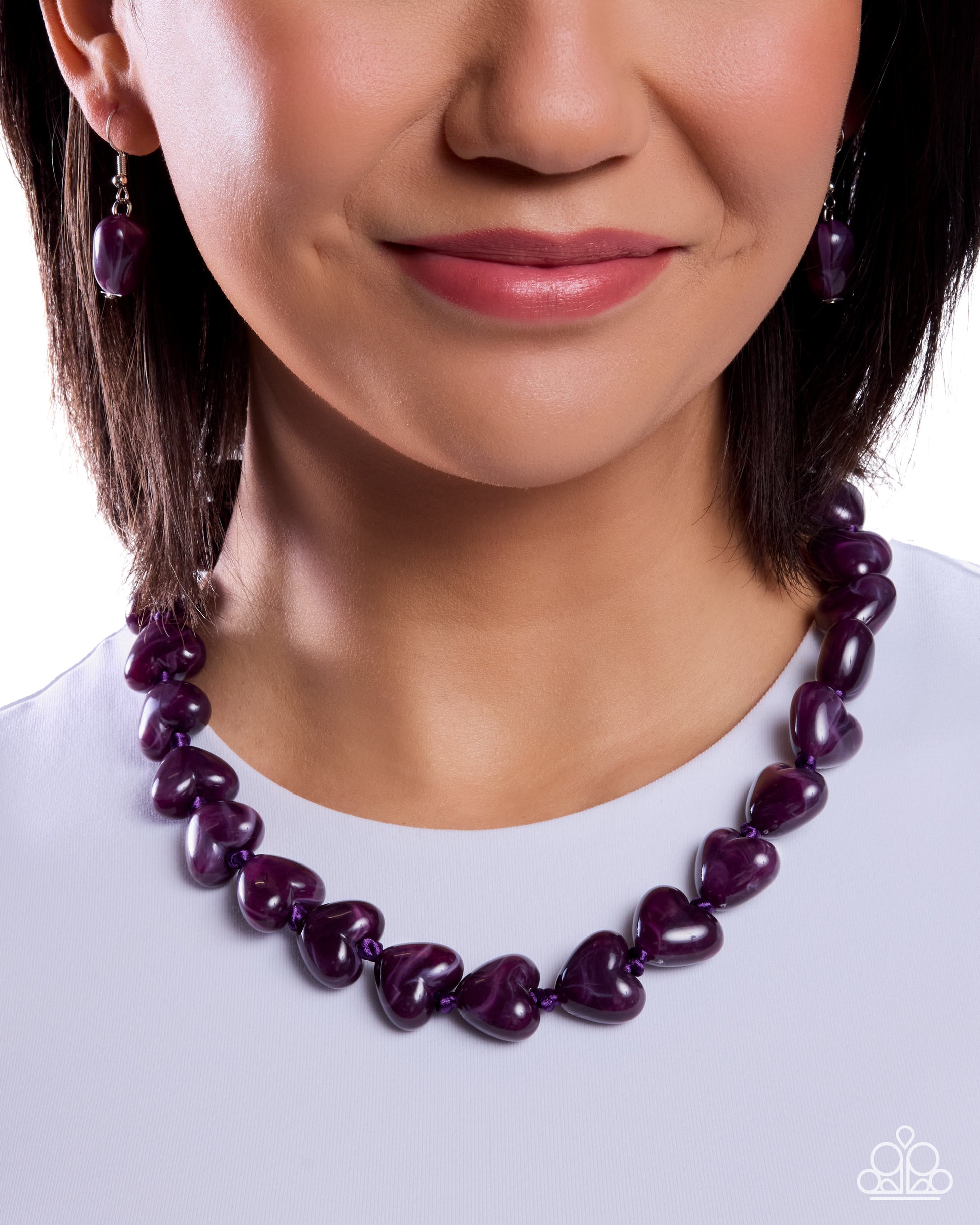 Close-up of a woman wearing a purple heart-shaped necklace and earrings on a white background