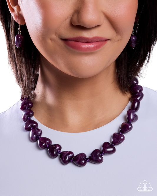 Close-up of a woman wearing a purple heart-shaped necklace and earrings on a white background