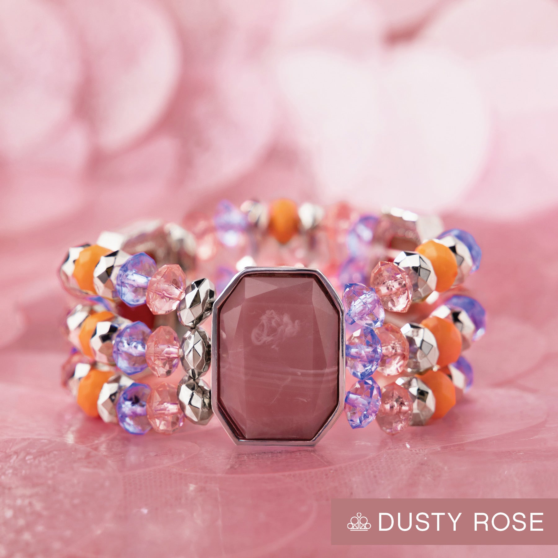 Colorful beaded bracelet with a pink gemstone on a pink background, featuring the brand 'Dusty Rose'.