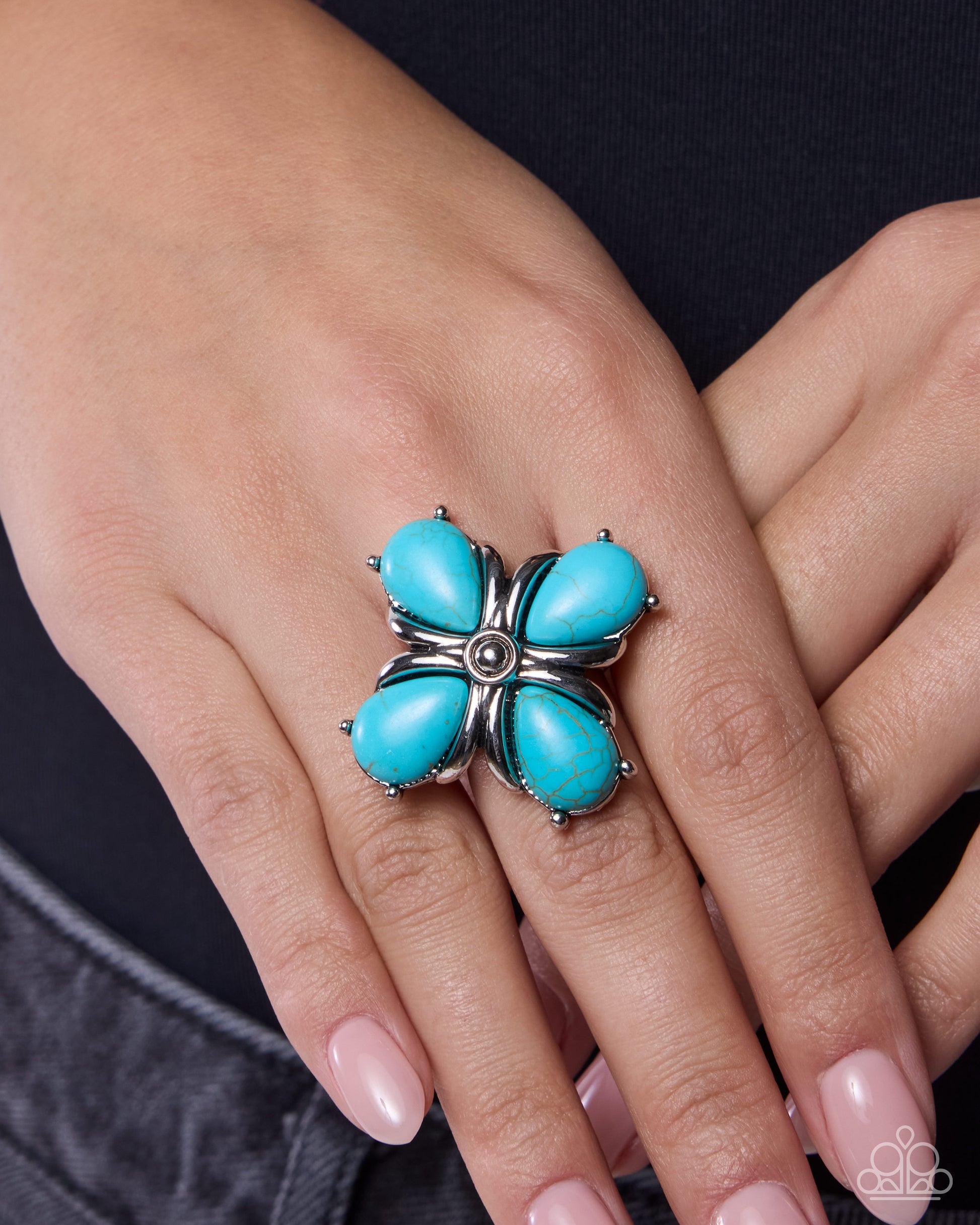 Turquoise flower-shaped ring on a person's finger against a neutral background