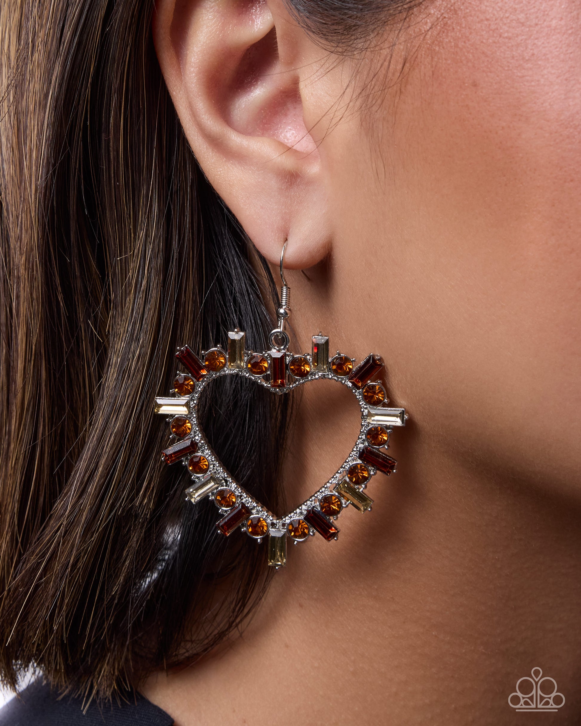 Heart-shaped earring with brown gemstones worn by a person