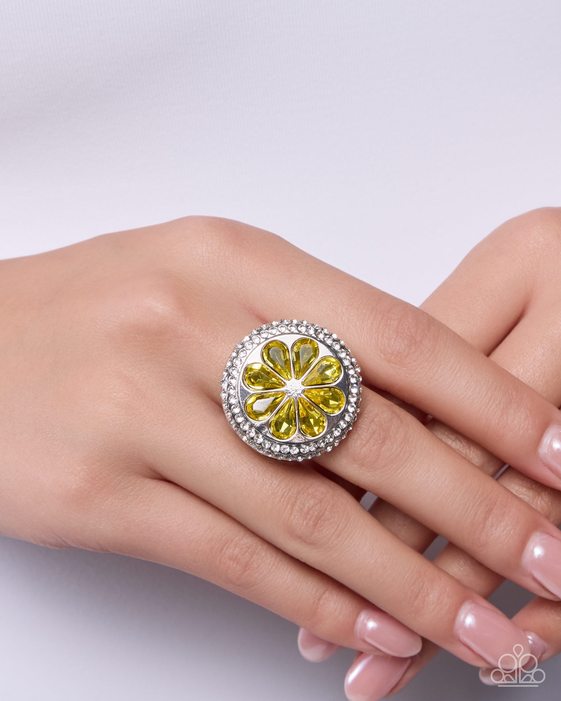Silver ring with yellow gemstones on a hand against a white background