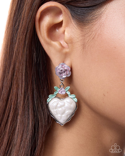 Close-up of an ear wearing a heart-shaped earring with floral details.