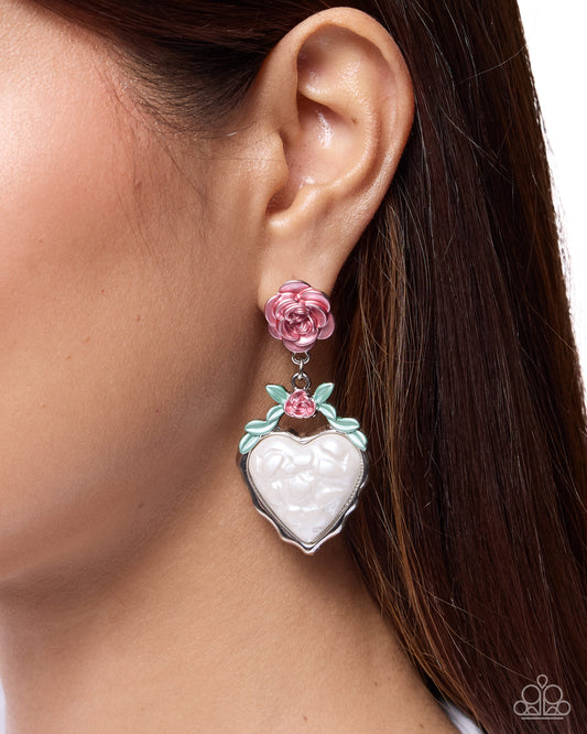 A close-up of a model's ear wearing a Paparazzi brand drop earring. The earring features a pink rose at the top, a small mint green leaf accent, and a dangling silver heart-shaped charm with a white textured center.