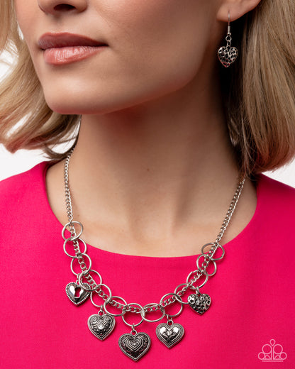 Woman wearing a silver necklace with heart charms on a pink background