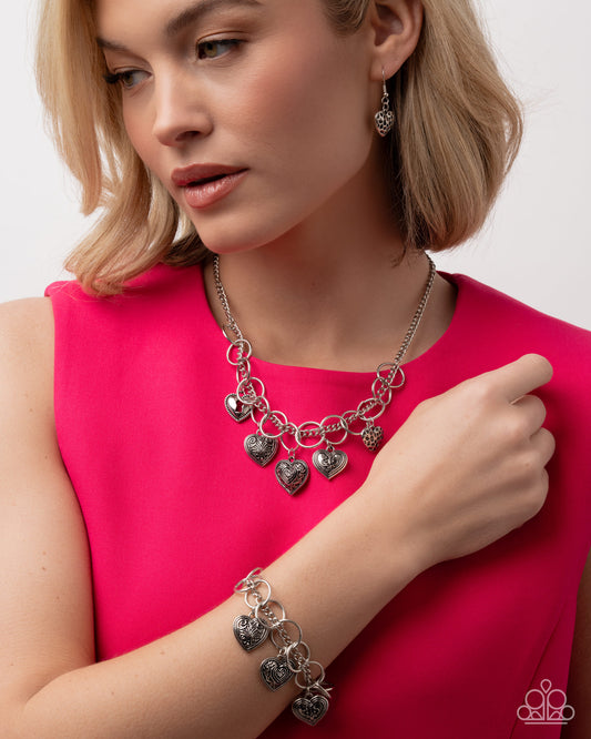 Woman wearing a silver charm bracelet and necklace against a white background