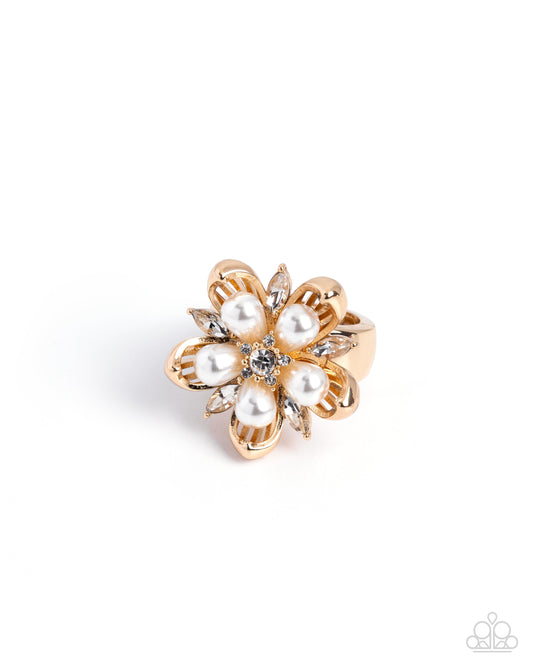 A gold flower-shaped ring featuring faux pearls as petals and a small clear crystal in the center, set against a plain white background.