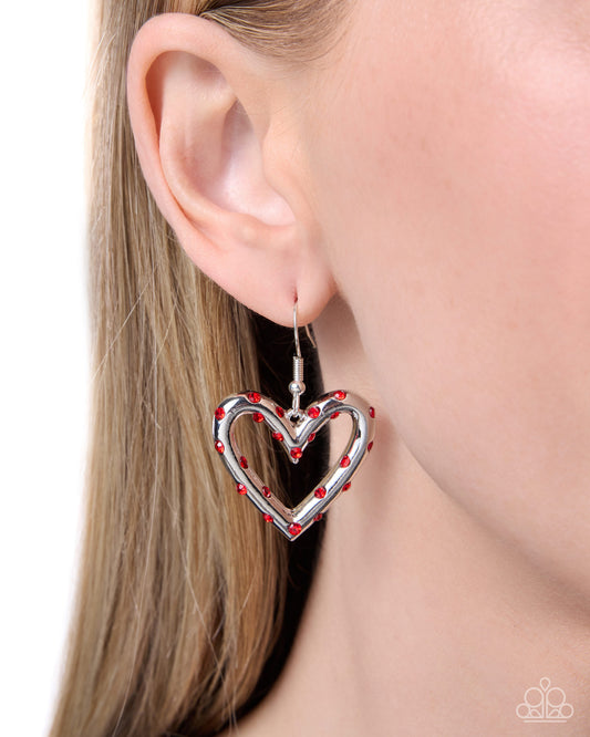 Heart-shaped earring with red embellishments worn by a model