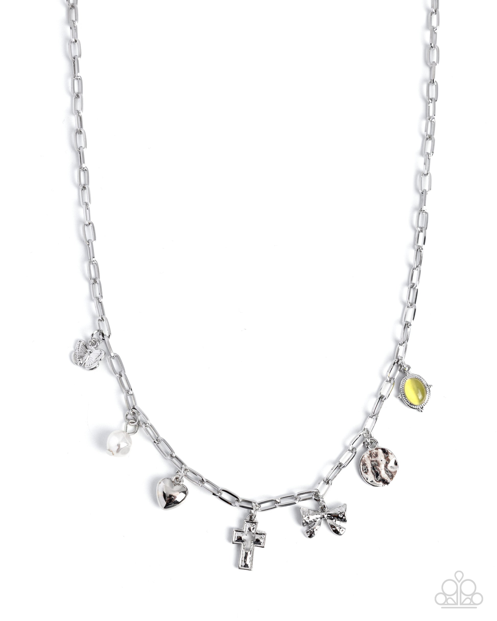 A silver paperclip chain necklace with dangling charms, including a cross, heart, bow, textured bead, and a small yellow-green leaf charm, shown on a plain white background.