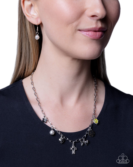 A close-up of a woman wearing a silver-toned charm necklace and matching drop earrings against a white background.