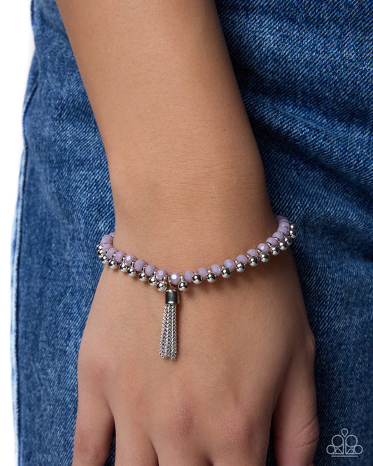 Pink beaded bracelet with a silver tassel on a wrist against a blue denim background