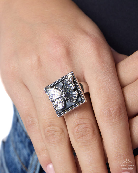 Silver butterfly ring on a person's finger with a blurred background