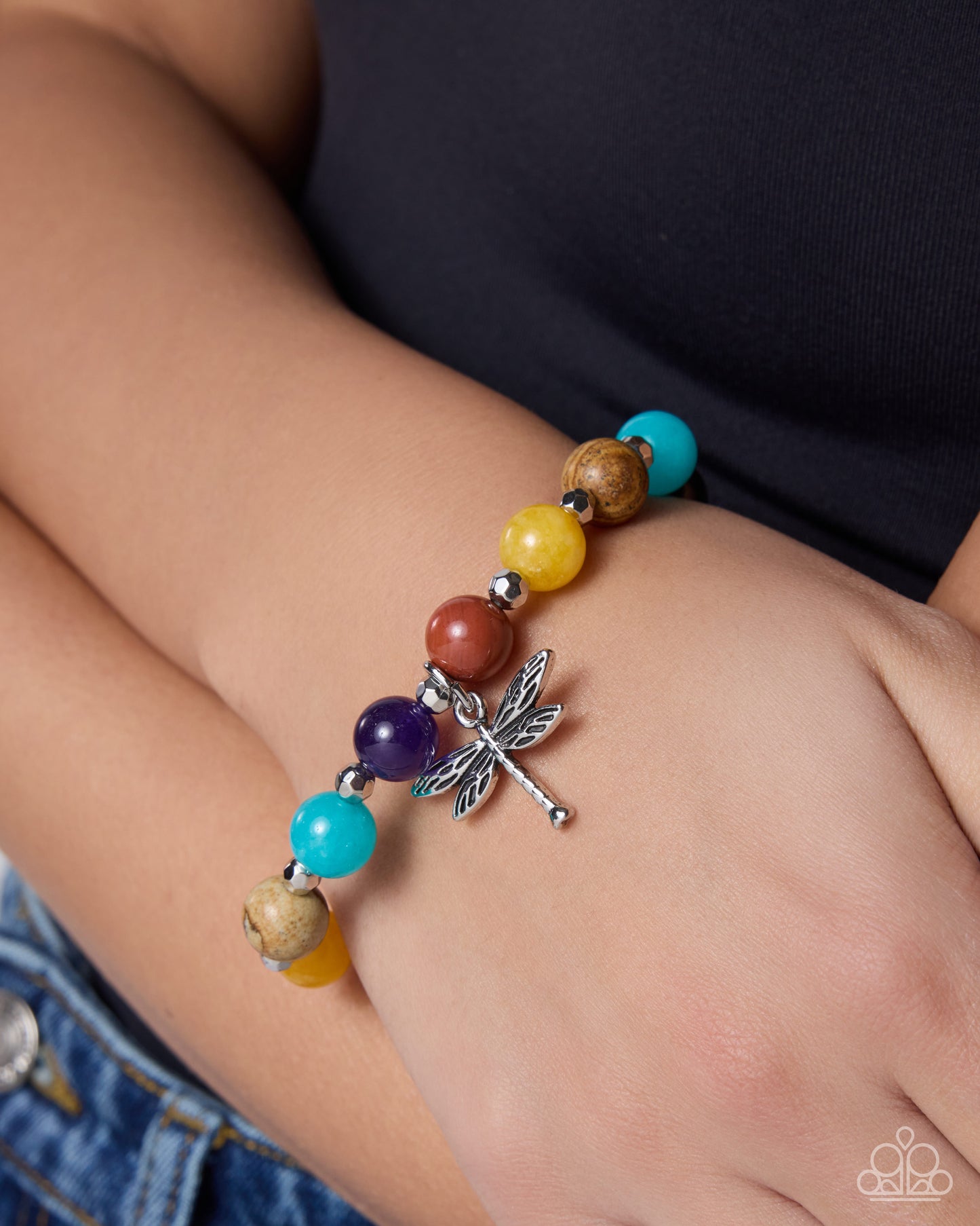 Colorful beaded bracelet with a dragonfly charm on a wrist.