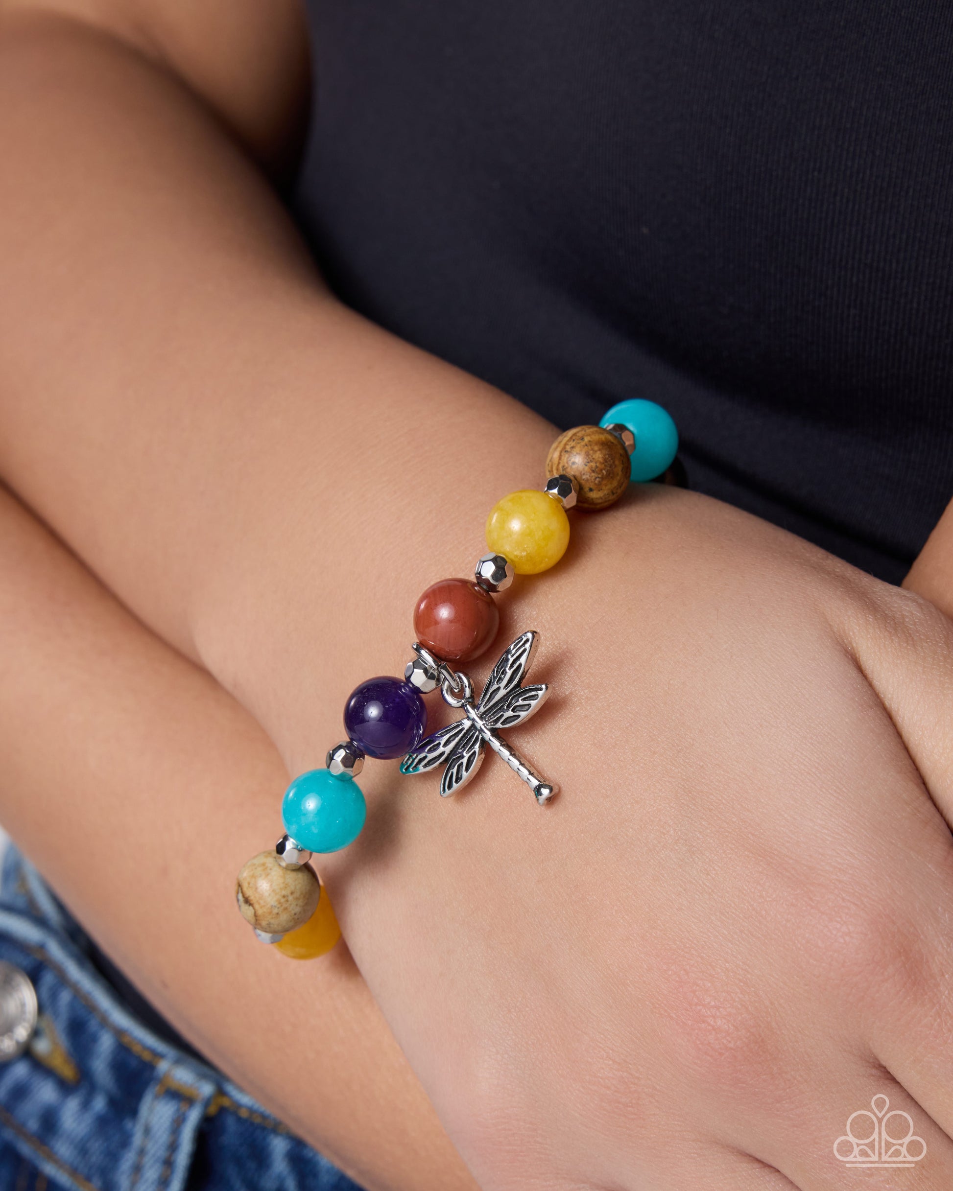 Colorful beaded bracelet with a dragonfly charm on a wrist.