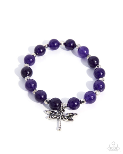 Purple beaded bracelet with a silver dragonfly charm on a white background