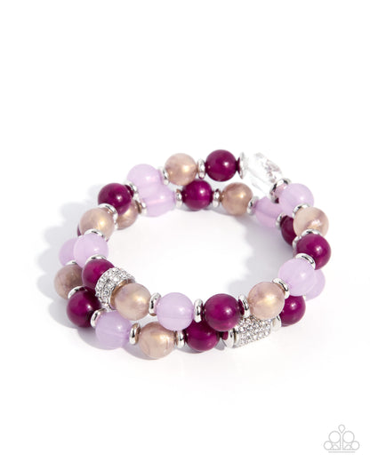 A multi-strand beaded bracelet featuring round beads in deep magenta, light lavender, and champagne beige, accented with silver spacer rings and a silver rhinestone-embellished charm, displayed on a clean white background.