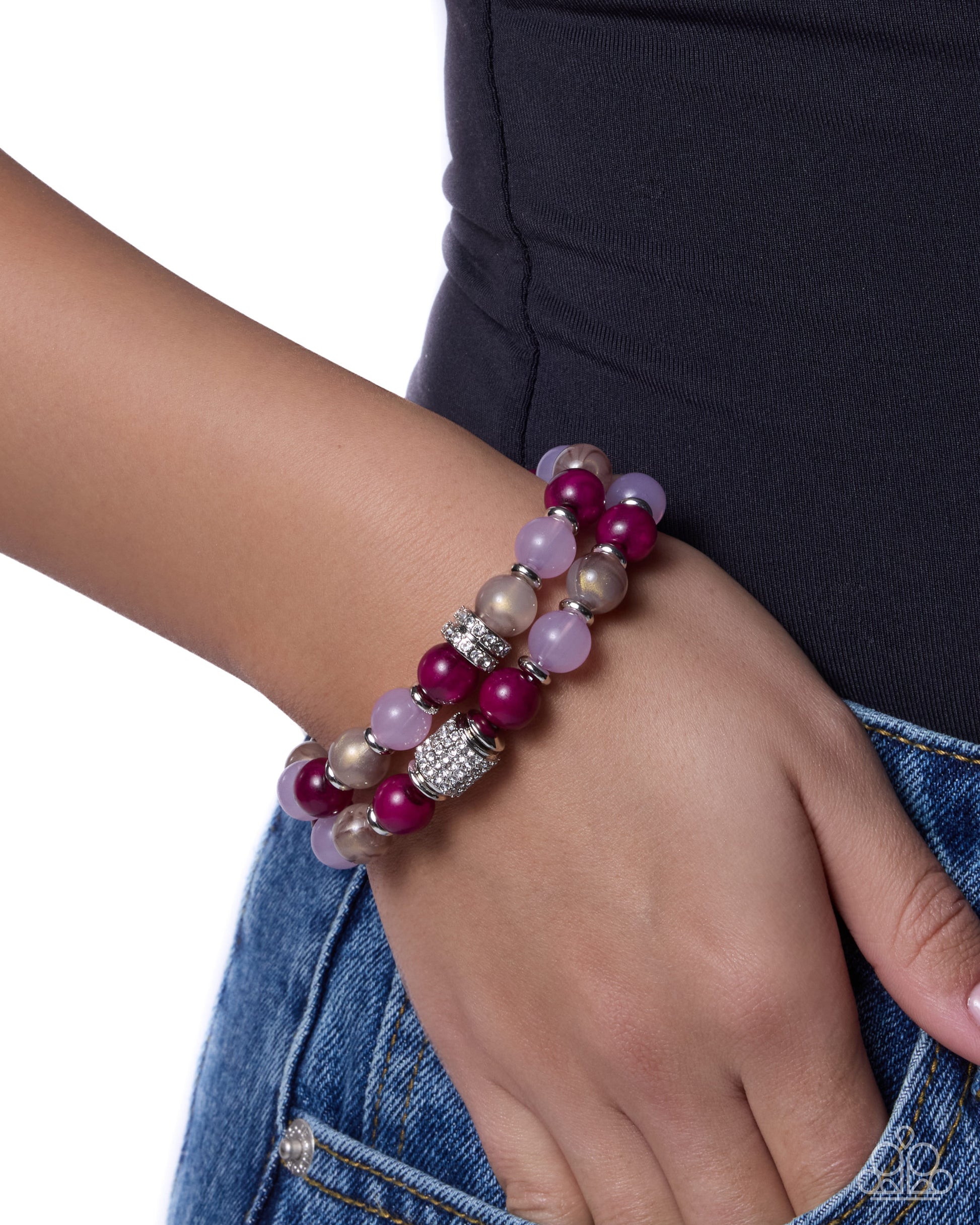 A close-up of a person's wrist wearing two beaded bracelets. The bracelets feature glossy magenta beads, pale lavender beads, and metallic champagne beads with a silver rhinestone-embellished spacer.