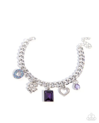 A silver-tone charm bracelet featuring multiple dangling charms, including a central rectangular purple gemstone, a heart-shaped crystal charm, a blue and white evil eye charm, and a small purple oval charm, shown on a plain white background.