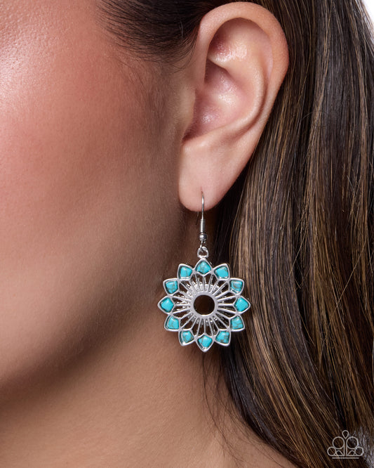 A close-up of a model's ear wearing a silver dangle earring with a turquoise blue floral pattern and a black center.