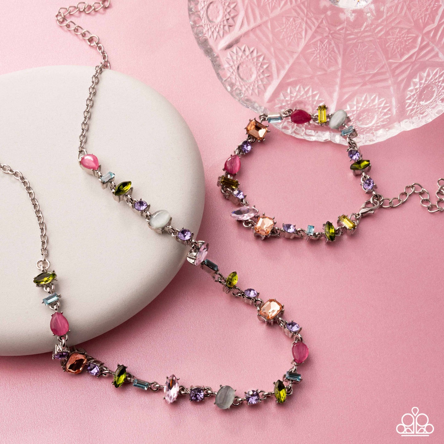 Colorful beaded necklace and bracelet on a pink surface with a white stone and decorative glass dish.