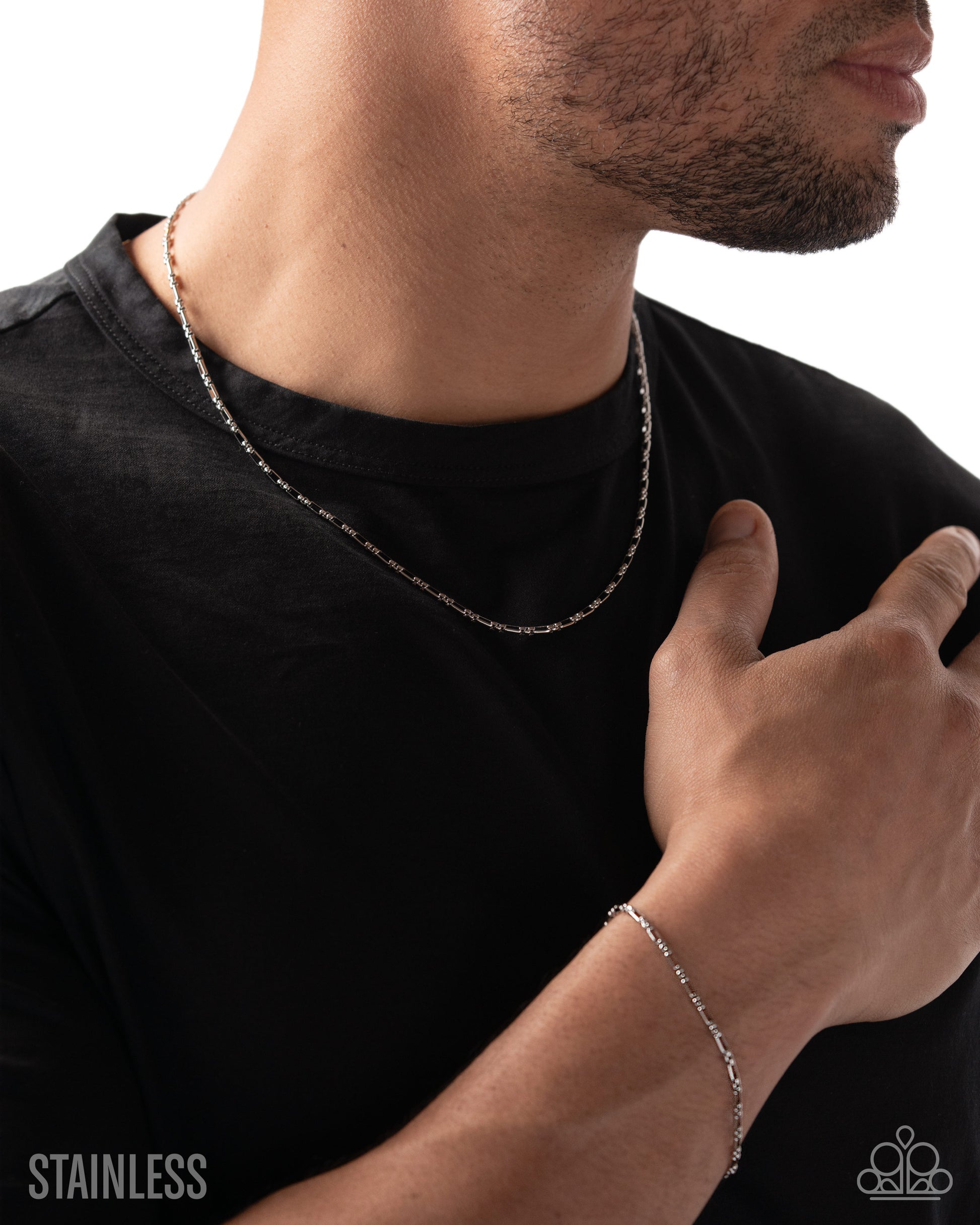 Man wearing a silver chain necklace and bracelet on a black shirt against a white background