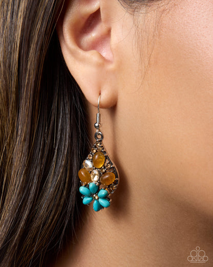 A close-up of a model's ear wearing a teardrop-shaped dangle earring with turquoise blue flower-like beads, amber-colored stones, and a silver-toned metal frame.