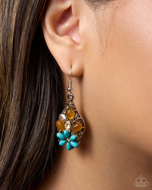 A close-up of a model's ear wearing a teardrop-shaped dangle earring with turquoise blue flower-like beads, amber-colored stones, and a silver-toned metal frame.