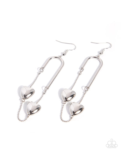 A pair of silver drop earrings featuring three-dimensional heart charms suspended from curved bar hooks, shown against a plain white background.