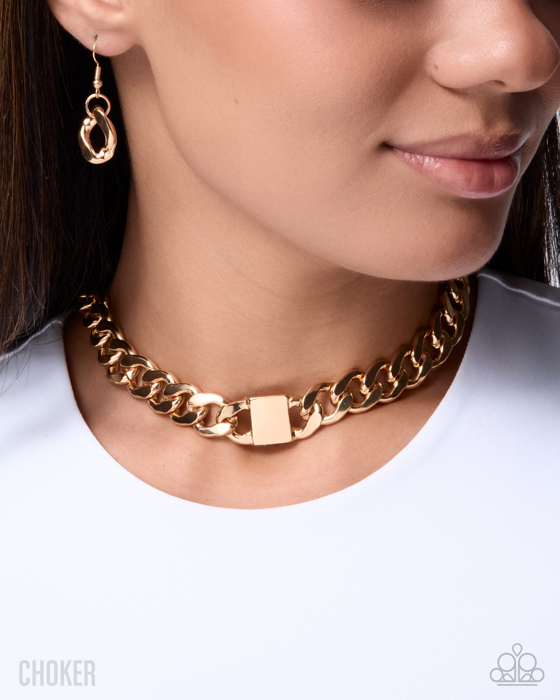 A close-up of a woman wearing a chunky gold chain choker necklace with a rectangular clasp, along with matching gold hoop earrings.