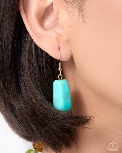 A close-up of a model's ear wearing a single drop earring with a turquoise rectangular stone and a gold fishhook wire.