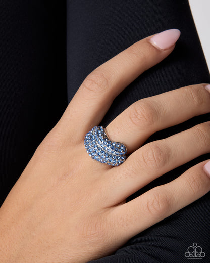 A close-up of a hand wearing a wide silver band ring set with multiple rows of sparkling light blue stones, resting against dark clothing.
