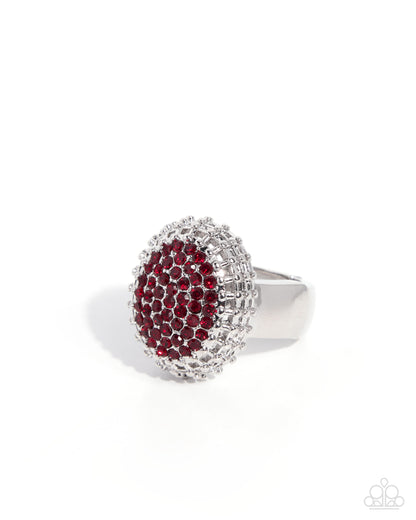 A silver-toned ring featuring a large oval face paved with deep red gemstones, surrounded by a halo of clear stones, set against a plain white background.