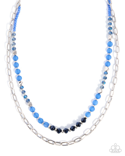 A double-strand beaded necklace featuring a silver paperclip chain and a layered strand of faceted beads in light blue, dark navy, and silver, displayed on a clean white background.