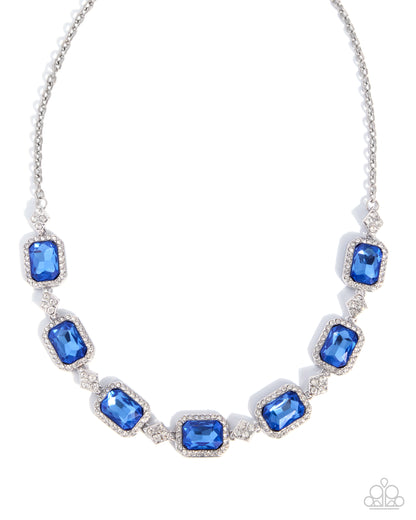 A silver-toned statement necklace featuring seven rectangular emerald-cut blue crystals in a halo setting, separated by small clear crystals, on a white background.