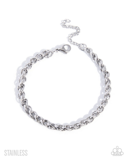A silver stainless steel curb chain bracelet with a lobster clasp and extender chain, displayed on a clean white background with 'STAINLESS' text in the lower left and a small logo in the lower right.